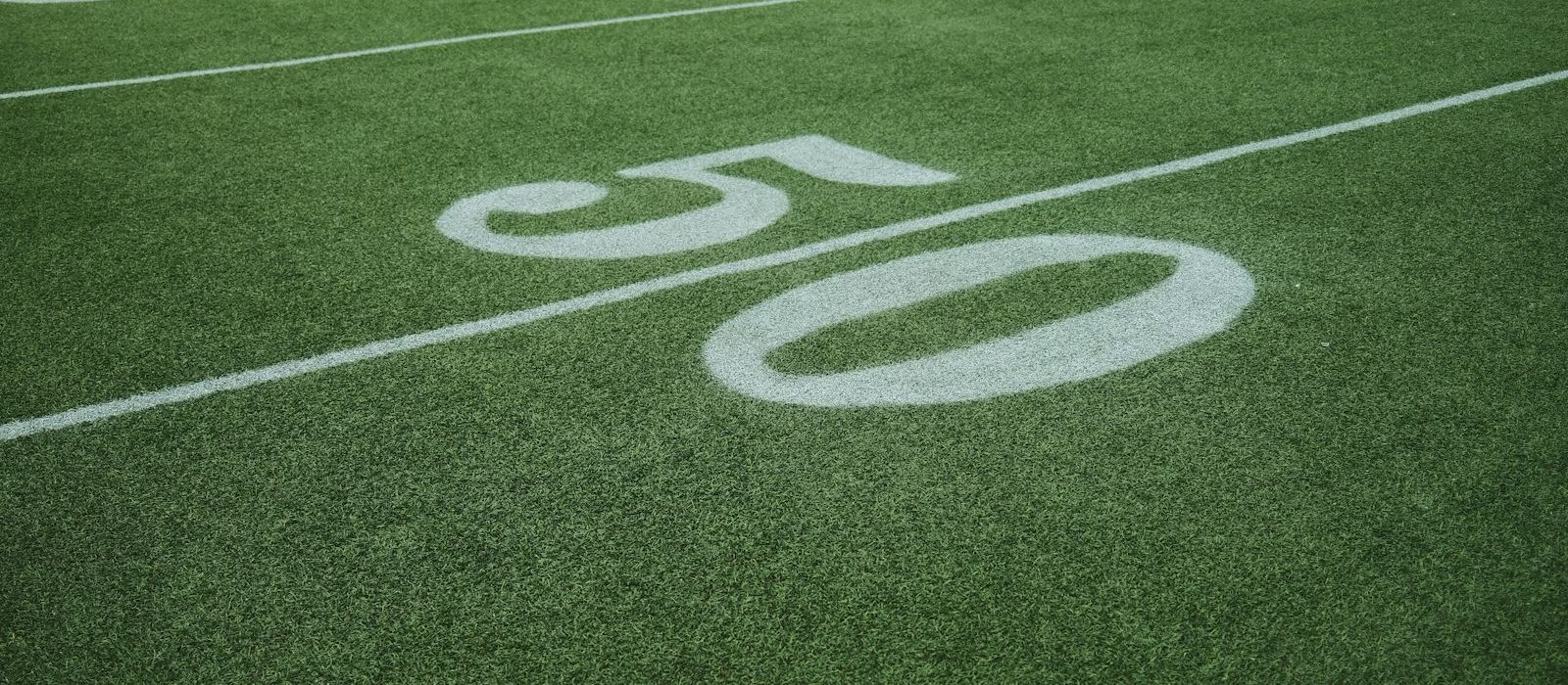 The fifty-yard line marked on the grass of an empty football ground with no crowd